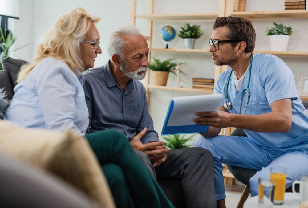 Profissional de saúde orientando casal de idosos durante atendimento home care em casa.